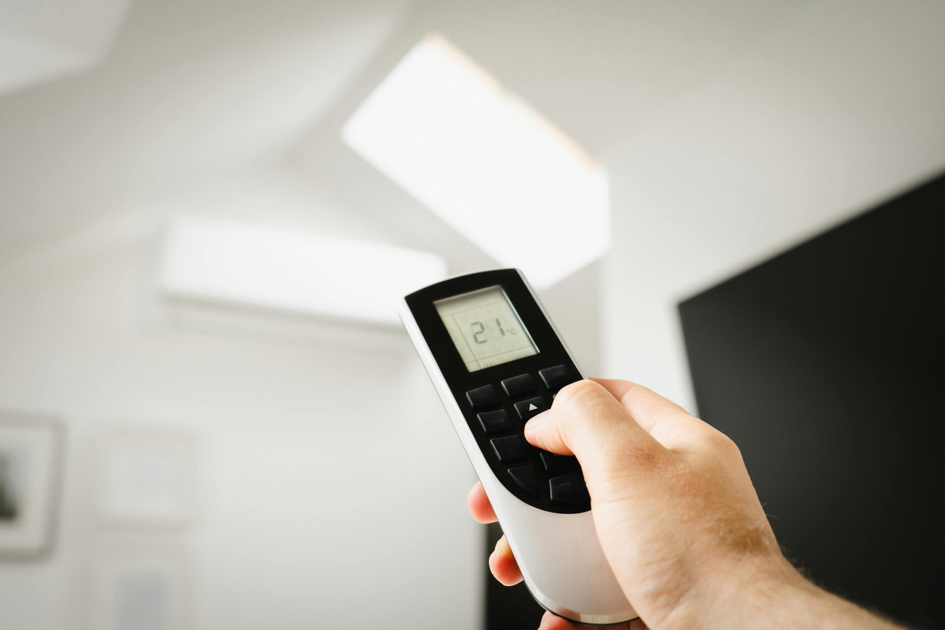 Primer plano de un hombre usando un control remoto para controlar el aire acondicionado en el interior de una vivienda.